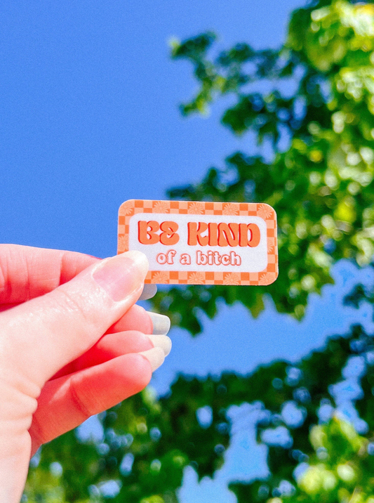 Retro orange checkered print with flowers that says "BE KIND OF A BITCH" in retro font